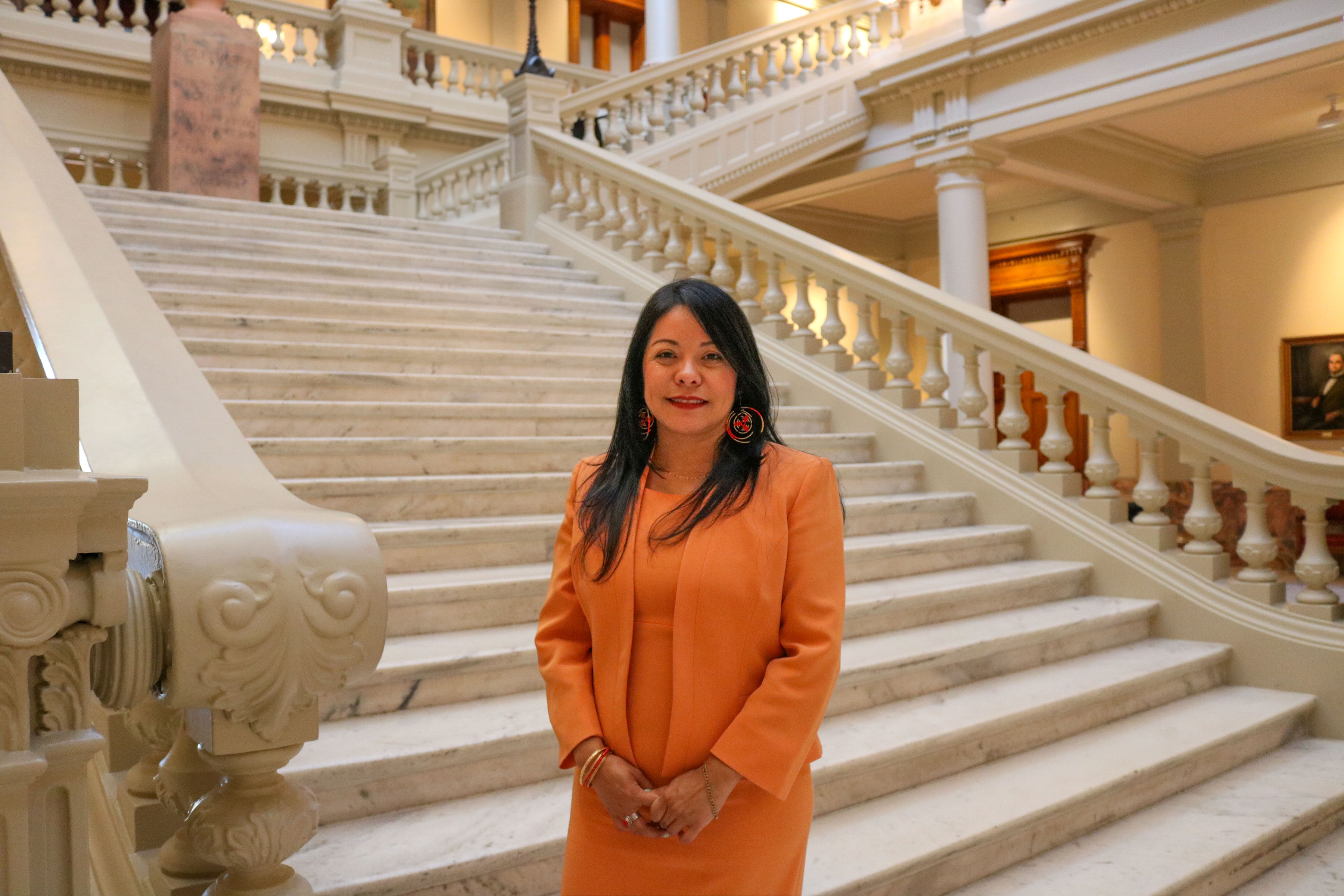 La abogada Brenda López Romero junto a una escalinata, vestida de naranja